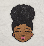 Embroidered patch of a child's face with  a afro puff hairstyle made of glitter
